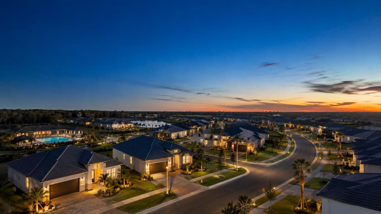 Aerial twilight view of a new home community in Tampa Bay with a pool, curving streets, and warmly lit homes